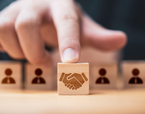 Hand putting hand shaking which print screen on wooden cube block in front of human icon for business deal and agreement concept.